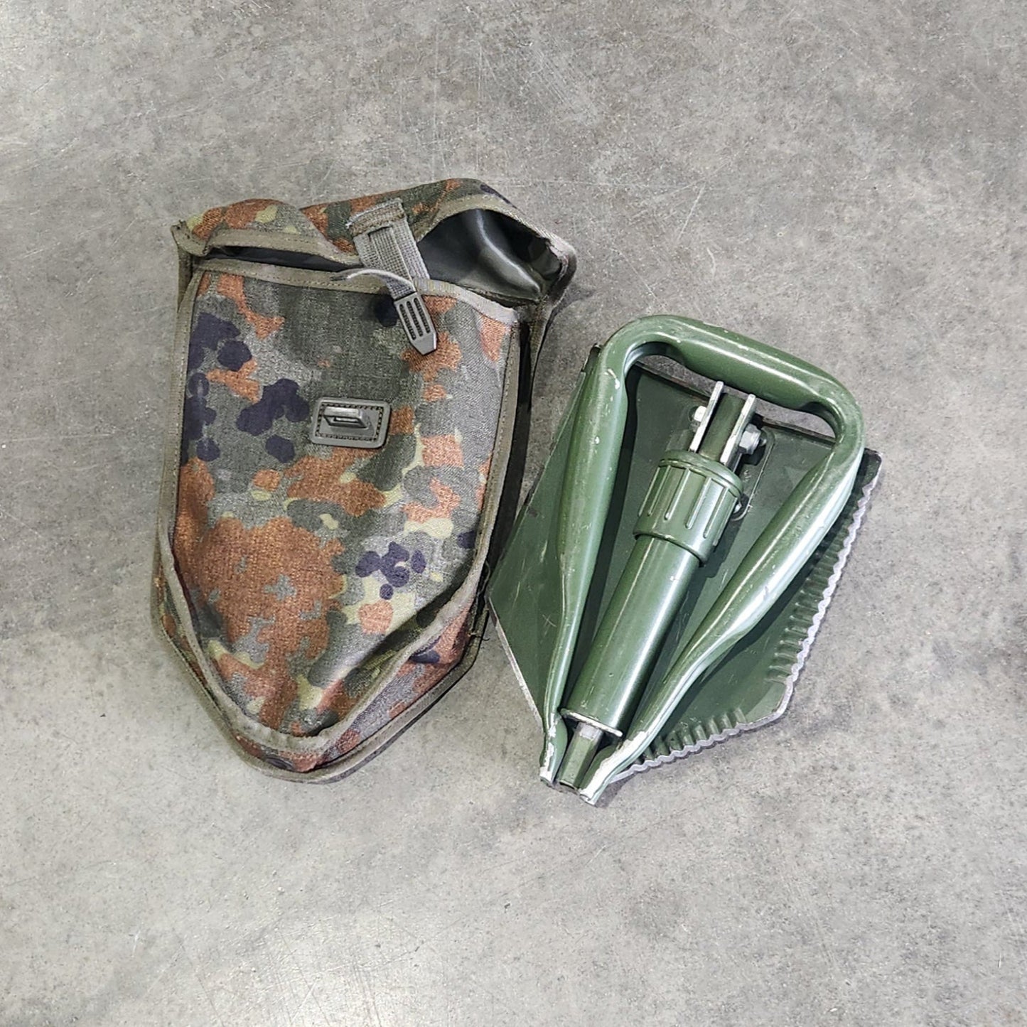Small camouflage tool and green container on a gray concrete surface
